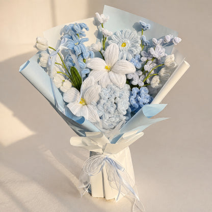 Blue and white handmade chenille flower bouquet with pale blue wrapping and a white ribbon on a warm neutral background.