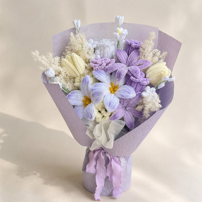 Lavender, pale blue and ivory handmade chenille flower bouquet with lilac wrapping and trailing ribbons on a warm ivory background.