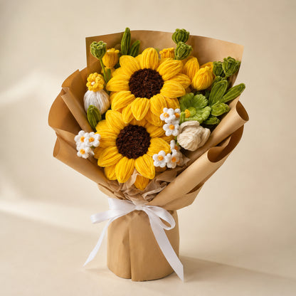 Yellow sunflower handmade chenille flower bouquet with white flowers, green foliage, tan wrapping and a white ribbon on a warm neutral background.