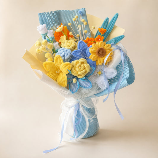 Blue, yellow and white handmade chenille flower bouquet with sunflower-style blooms, pale blue wrapping and blue ribbons on a warm neutral background.