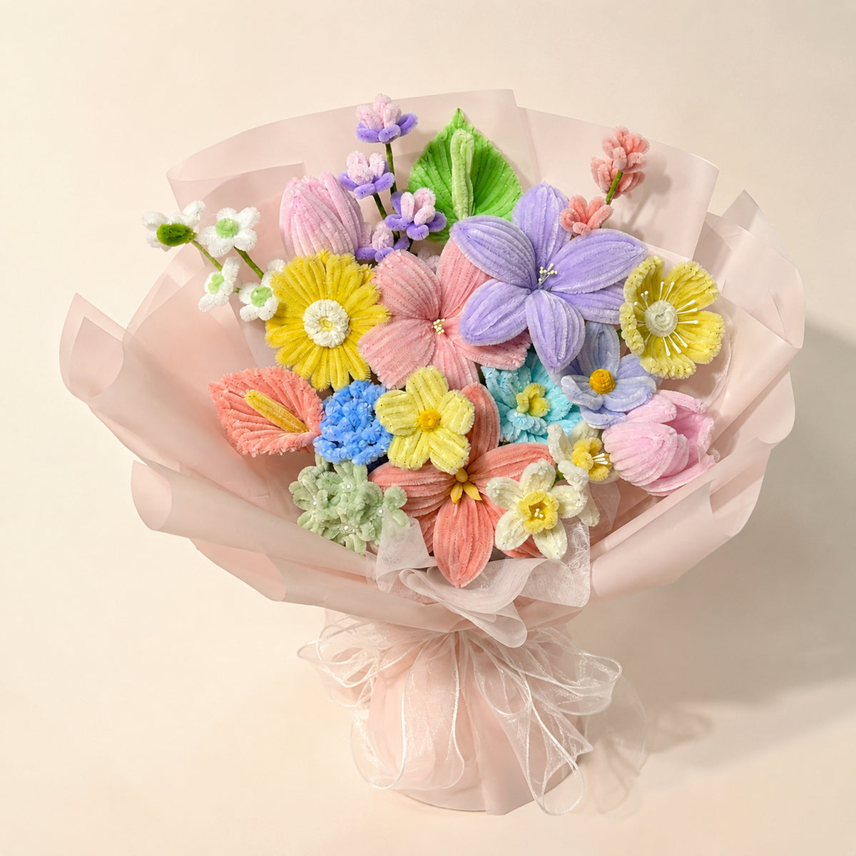 Pastel purple, pink, yellow and blue handmade chenille flower bouquet with blush wrapping and sheer ribbons on a warm neutral background.