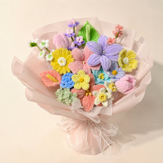 Pastel purple, pink, yellow and blue handmade chenille flower bouquet with blush wrapping and sheer ribbons on a warm neutral background.