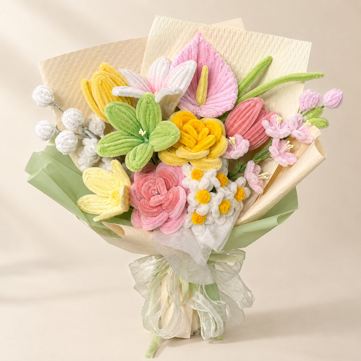 Pastel pink, yellow, green and ivory handmade chenille flower bouquet with cream and pale green wrapping on a warm neutral background.